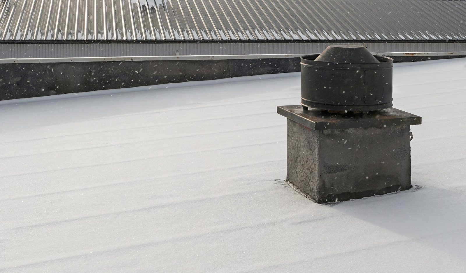 Ventilatiekap op een plat dak tijdens sneeuwval